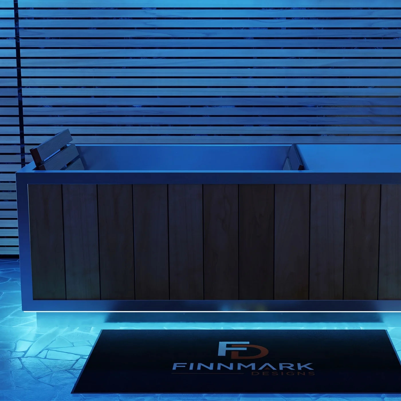 A modern rectangular outdoor bathtub with a dark wood-paneled front and stainless steel sides, shown under blue ambient lighting. A black doormat with the FINMARK DESIGNS logo is placed in front.